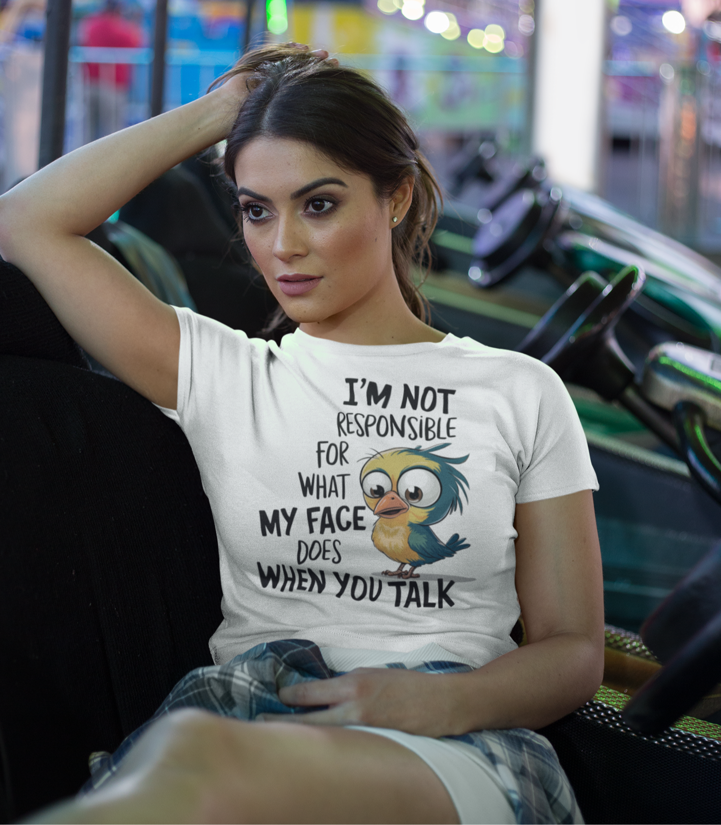 Γυναίκα φοράει λευκό crop top με αστείο σχέδιο πουλιού και φράση "I’m not responsible for what my face does when you talk", ενώ κάθεται σε παιχνίδι λούνα παρκ.