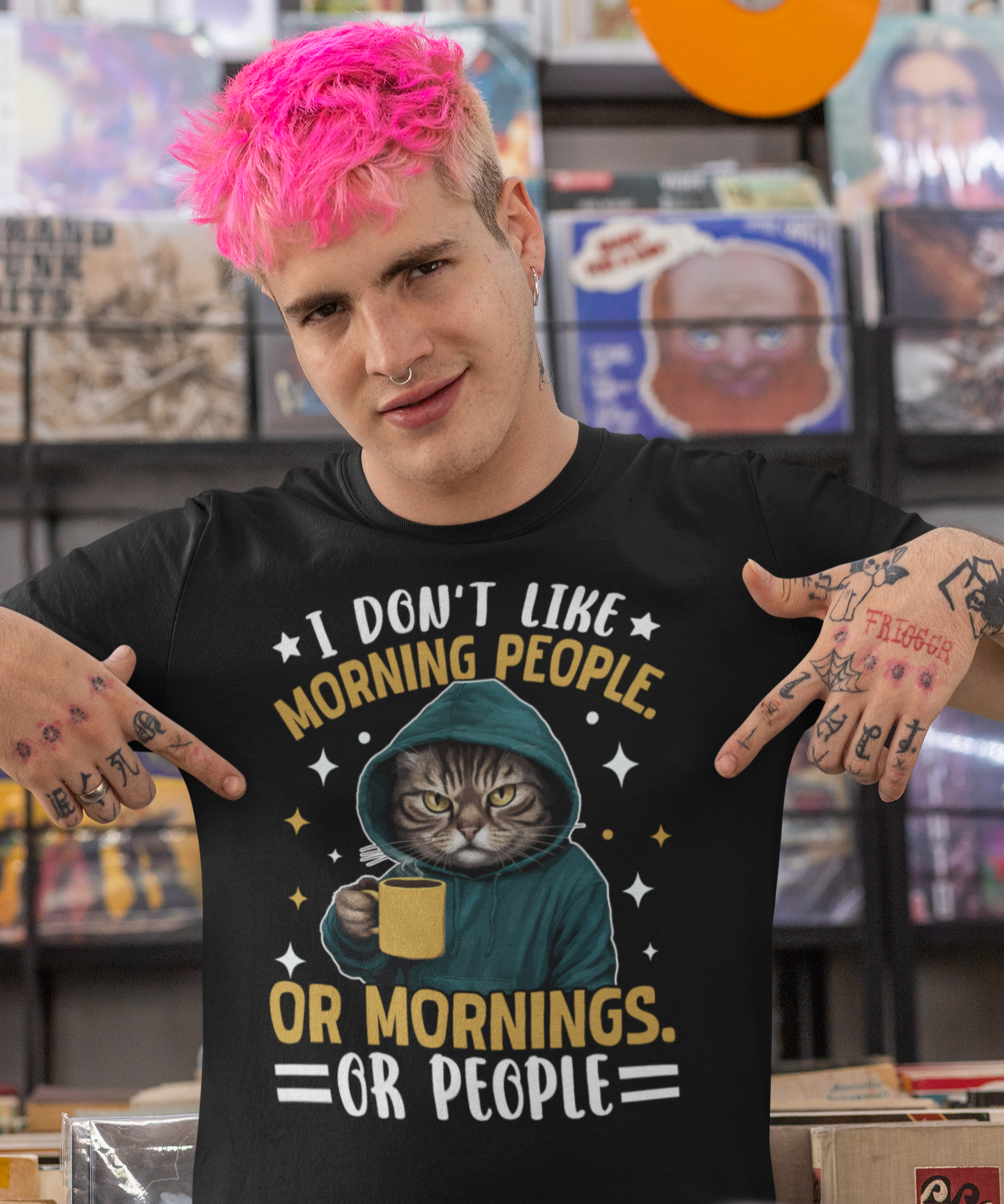Άνδρας με ροζ μαλλιά και τατουάζ δείχνει το μαύρο μπλουζάκι του με αστείο σχέδιο γάτας και φράση “I Don’t Like Morning People. Or Mornings. Or People”