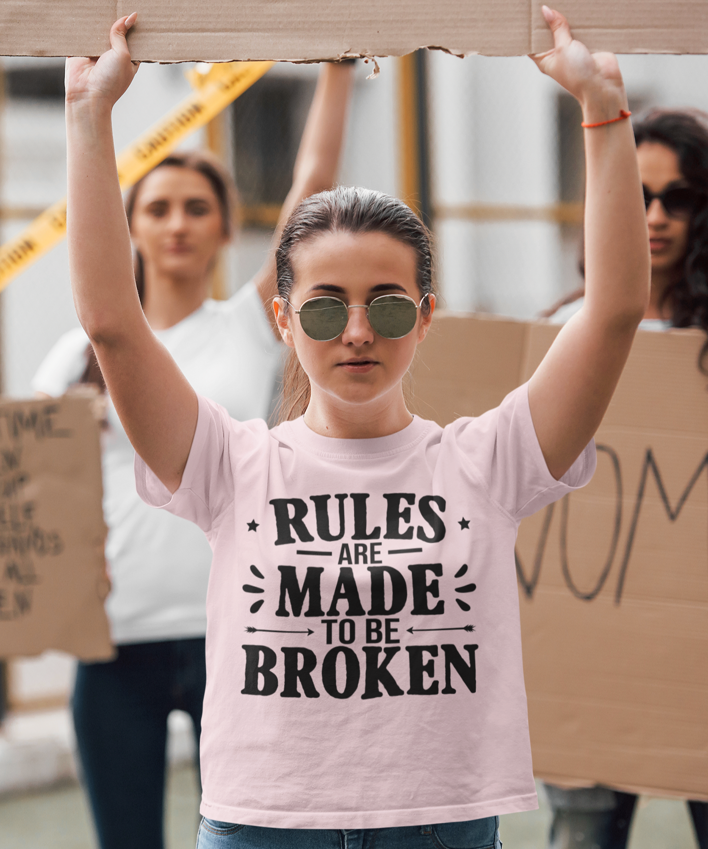 Γυναικείο ροζ T-shirt με μαύρη στάμπα "Rules Are Made To Be Broken", φορεμένο από γυναίκα σε διαδήλωση.