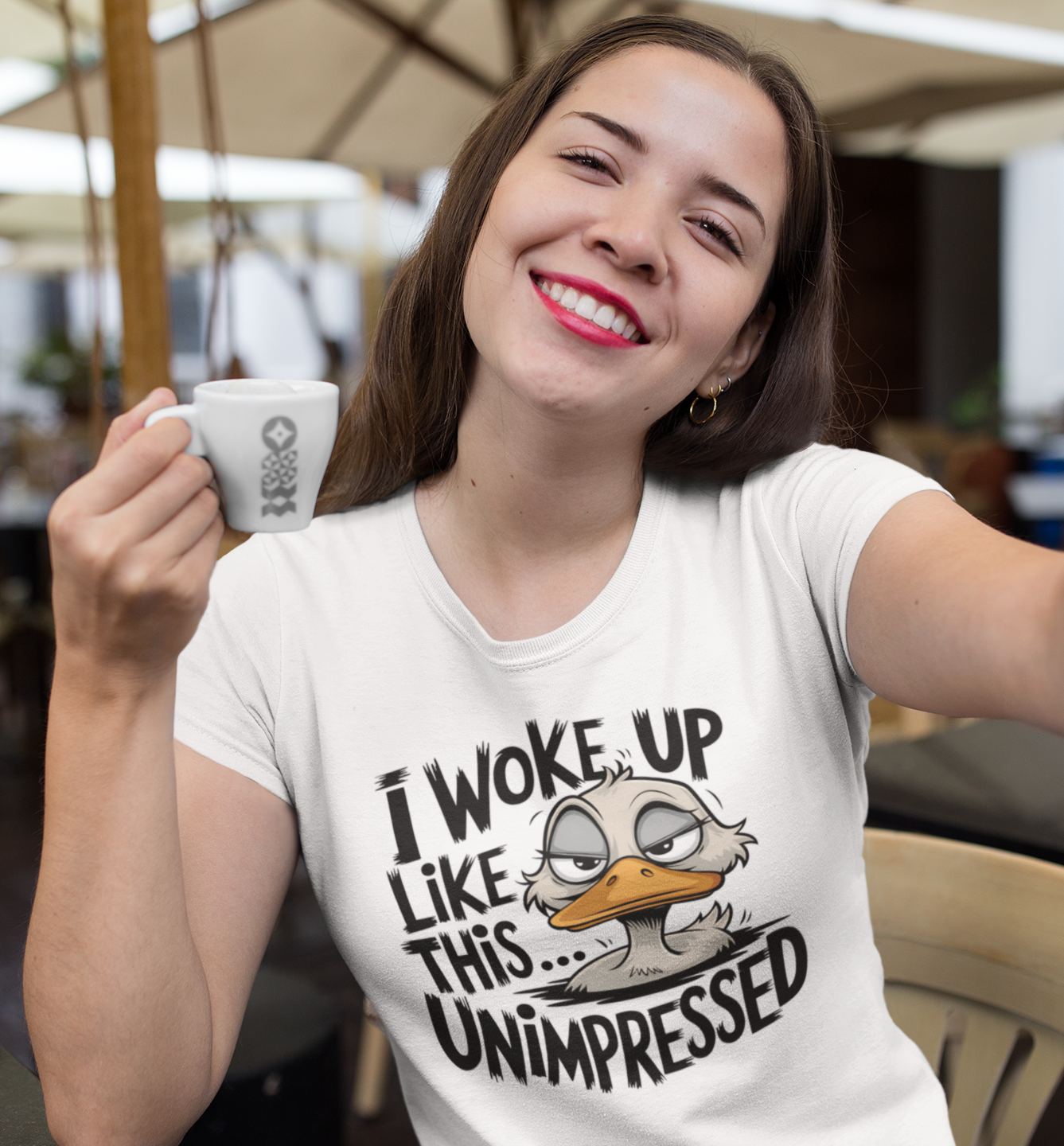 Γυναίκα σε καφέ κρατάει φλιτζάνι και φοράει t-shirt με σκίτσο πάπιας και τη φράση "I Woke Up Like This... Unimpressed"