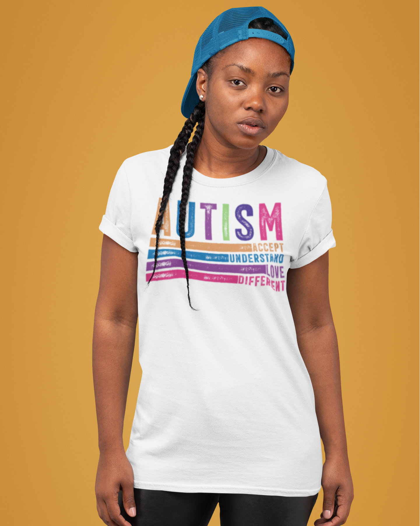 Γυναίκα με λευκό μπλουζάκι που γράφει "Autism: Accept, Understand, Love, Different" σε πολύχρωμο σχέδιο, μπροστά από πορτοκαλί φόντο, φορώντας μπλε καπέλο.