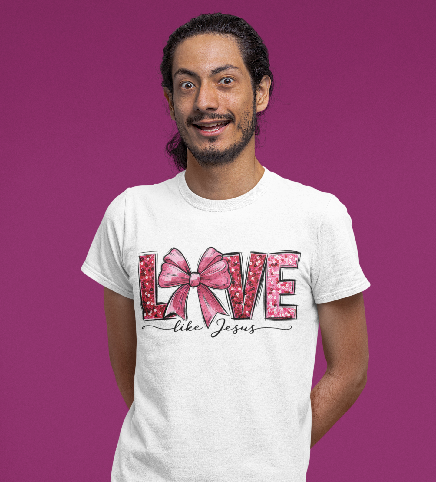 λευκό μπλουζάκι που γράφει "Love like Jesus" με ροζ φιόγκο, ποζάρει μπροστά σε μωβ φόντο με χαμογελαστή έκφραση.