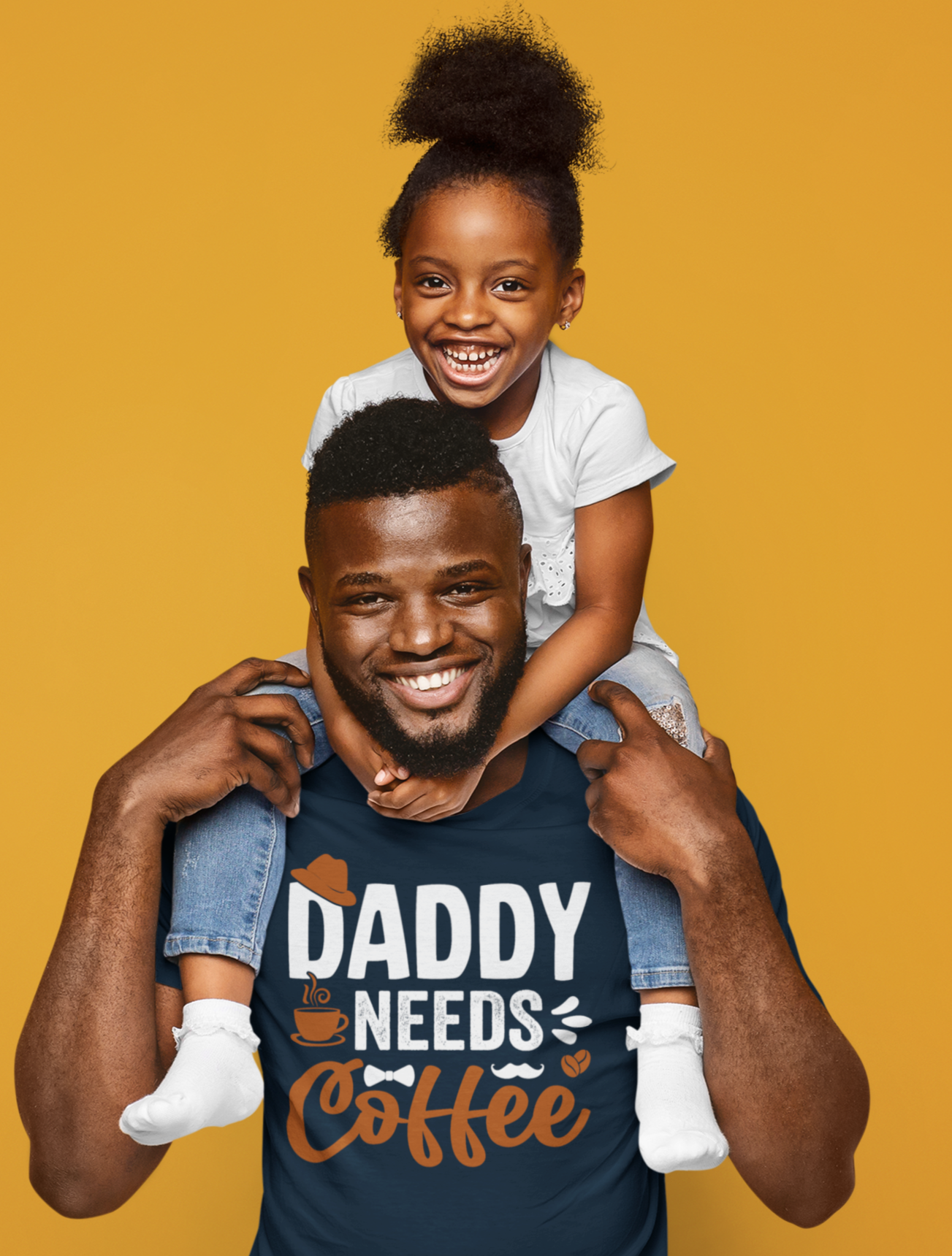 Πατέρας με μπλουζάκι “Daddy Needs Coffee” κρατά στην πλάτη του την κόρη του, και οι δύο χαμογελούν μπροστά σε κίτρινο φόντο.