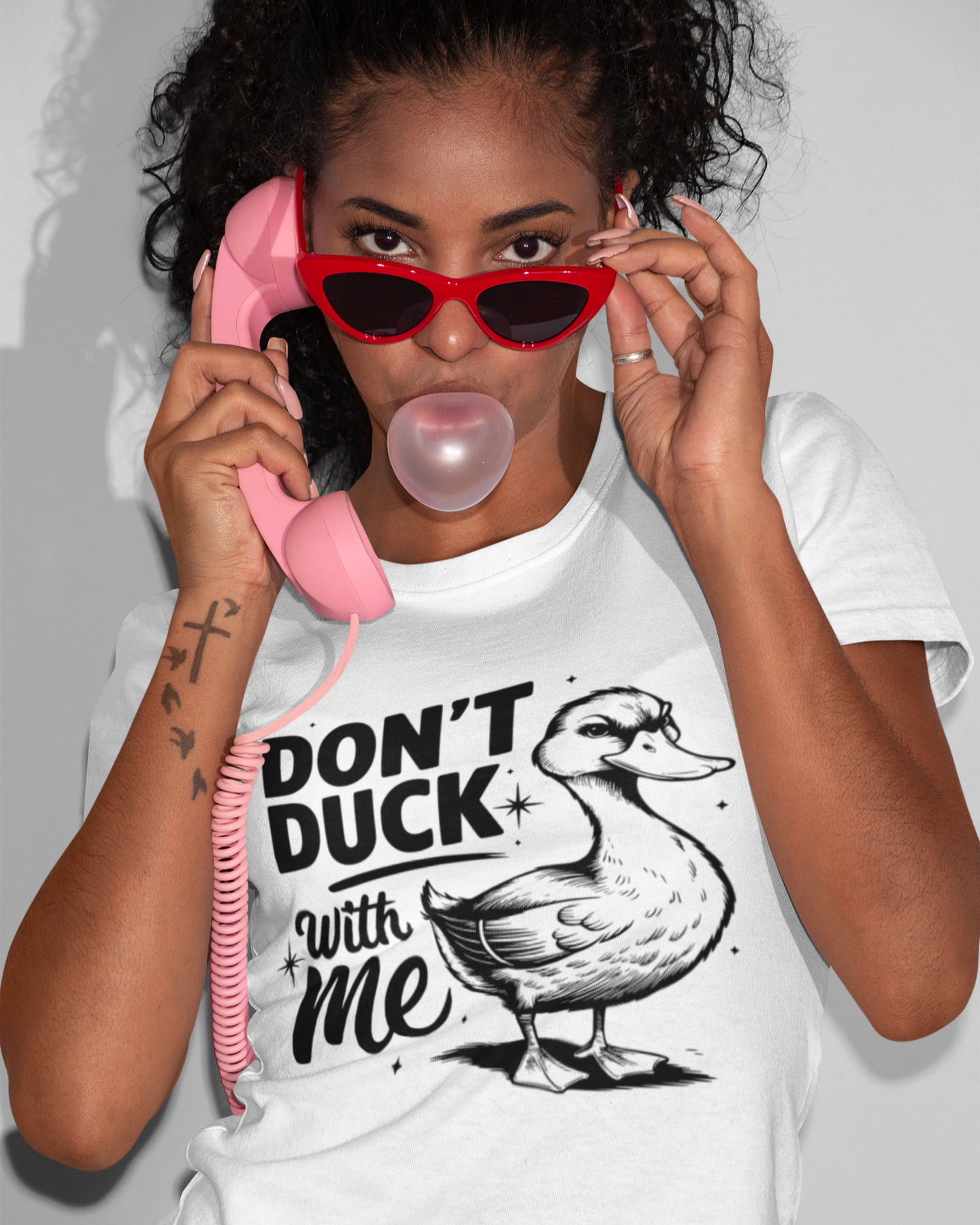 Γυναίκα με λευκό μπλουζάκι που γράφει "Don’t Duck With Me" με σχέδιο πάπια, φορά κόκκινα γυαλιά και κρατά ροζ τηλέφωνο, φουσκώνοντας τσίχλα.