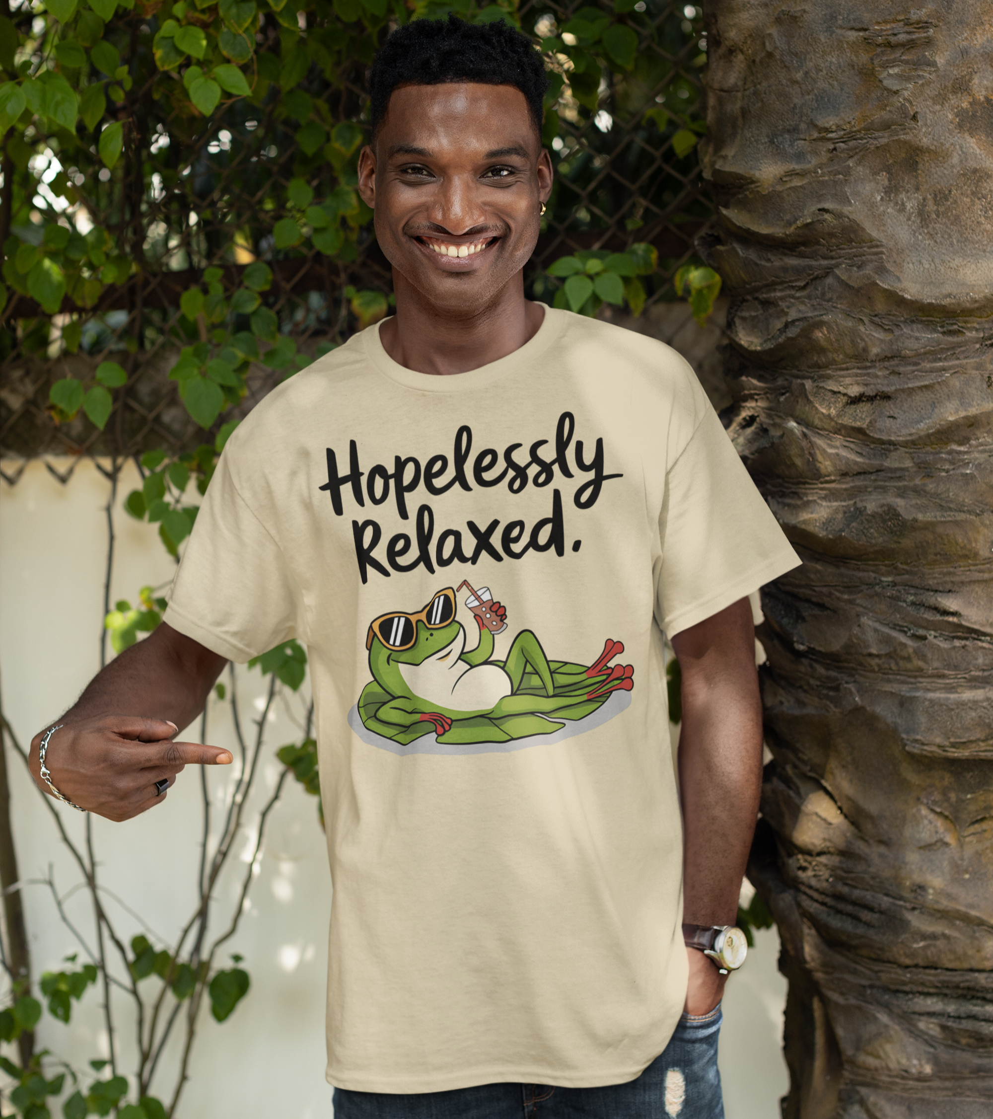 Άντρας με μπεζ μπλουζάκι “Hopelessly Relaxed” που δείχνει ένα βάτραχο ξαπλωμένο με γυαλιά και ποτό