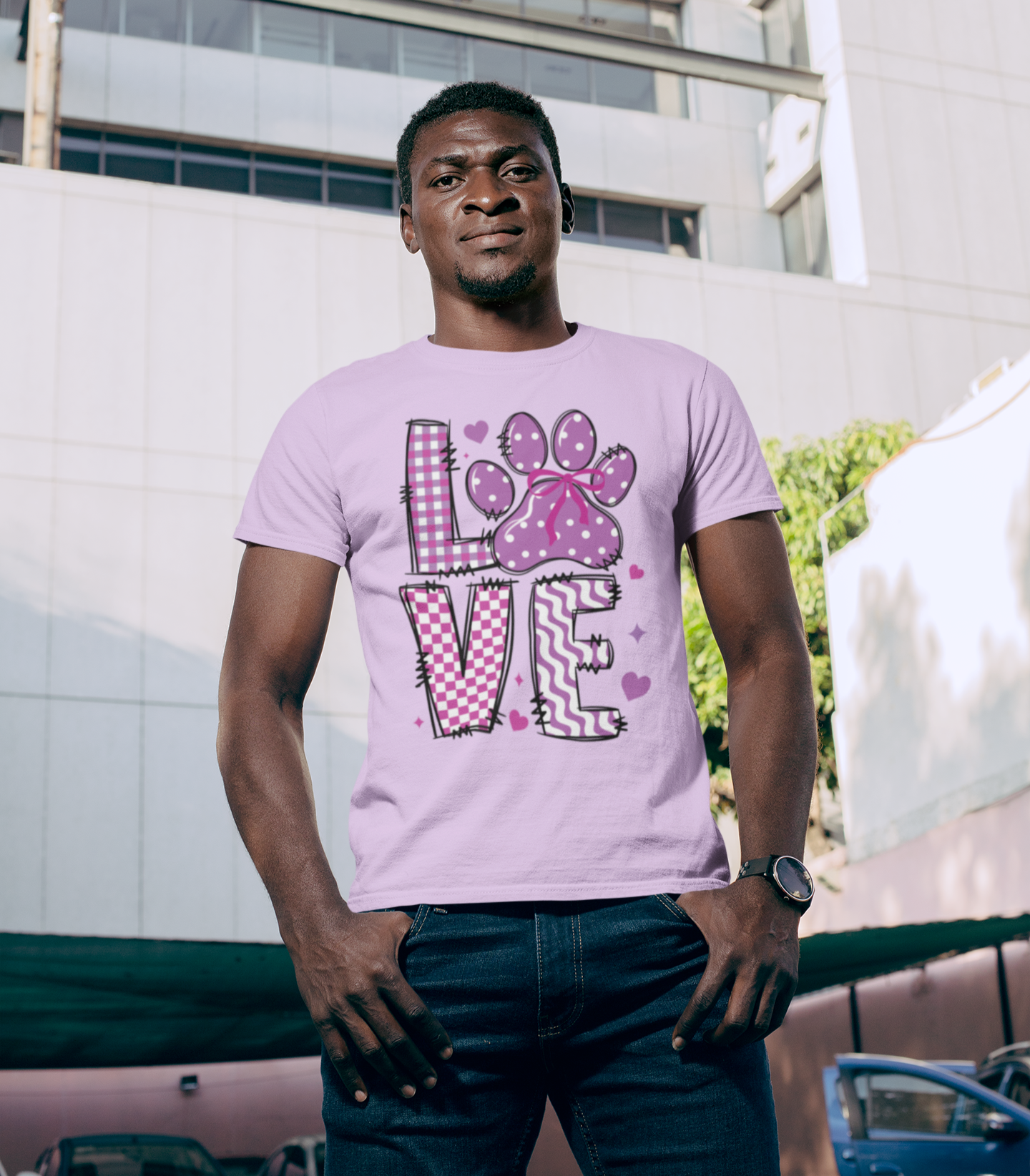 Άνδρας με μωβ μπλουζάκι και σχέδιο LOVE με πατουσάκι σε ροζ χρώμα, μπροστά από μοντέρνο κτίριο στην πόλη.