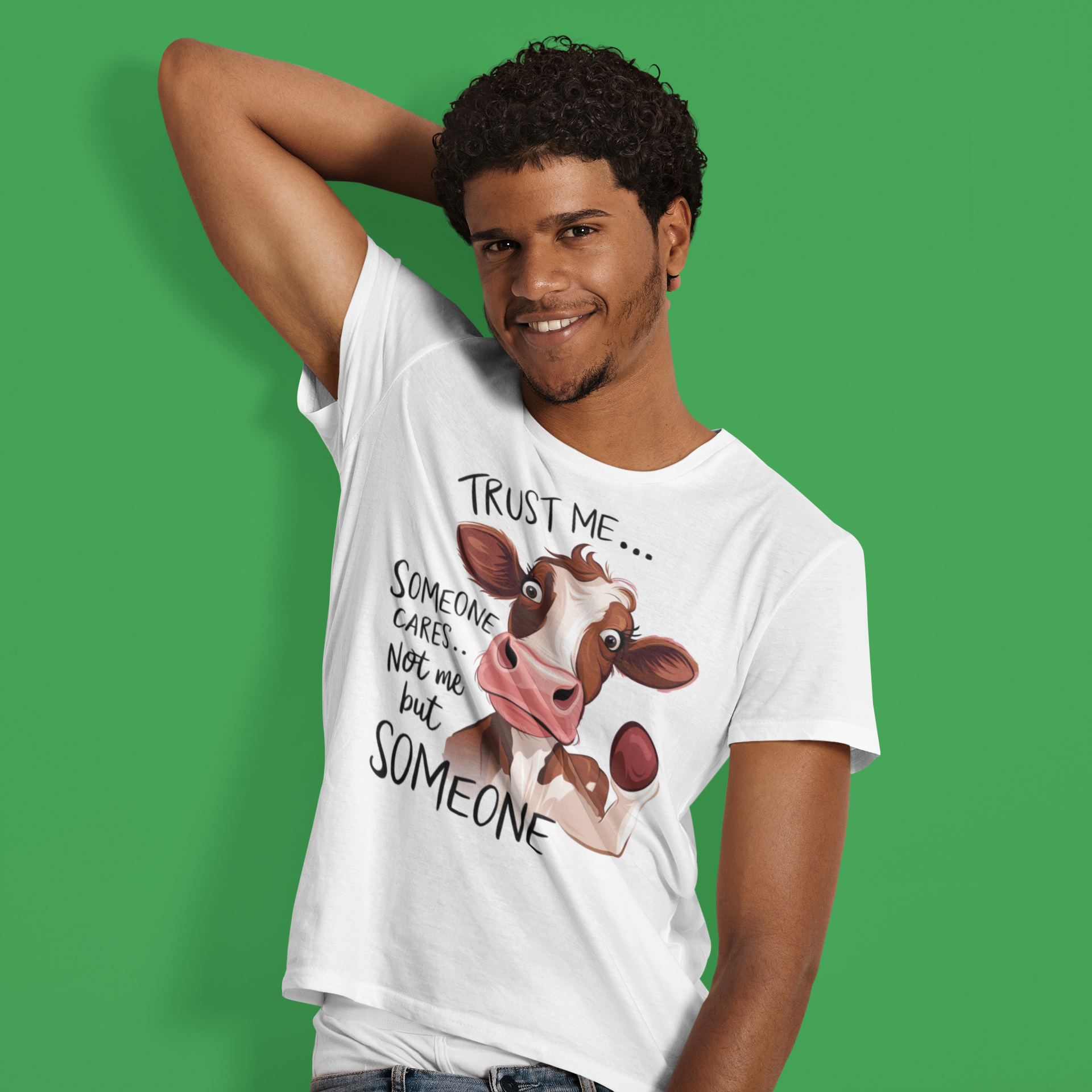 Άνδρας με λευκό μπλουζάκι που γράφει "Trust me… Someone cares… Not me but someone" και έχει σχέδιο σαρκαστικής αγελάδας, ποζάρει μπροστά σε πράσινο φόντο.