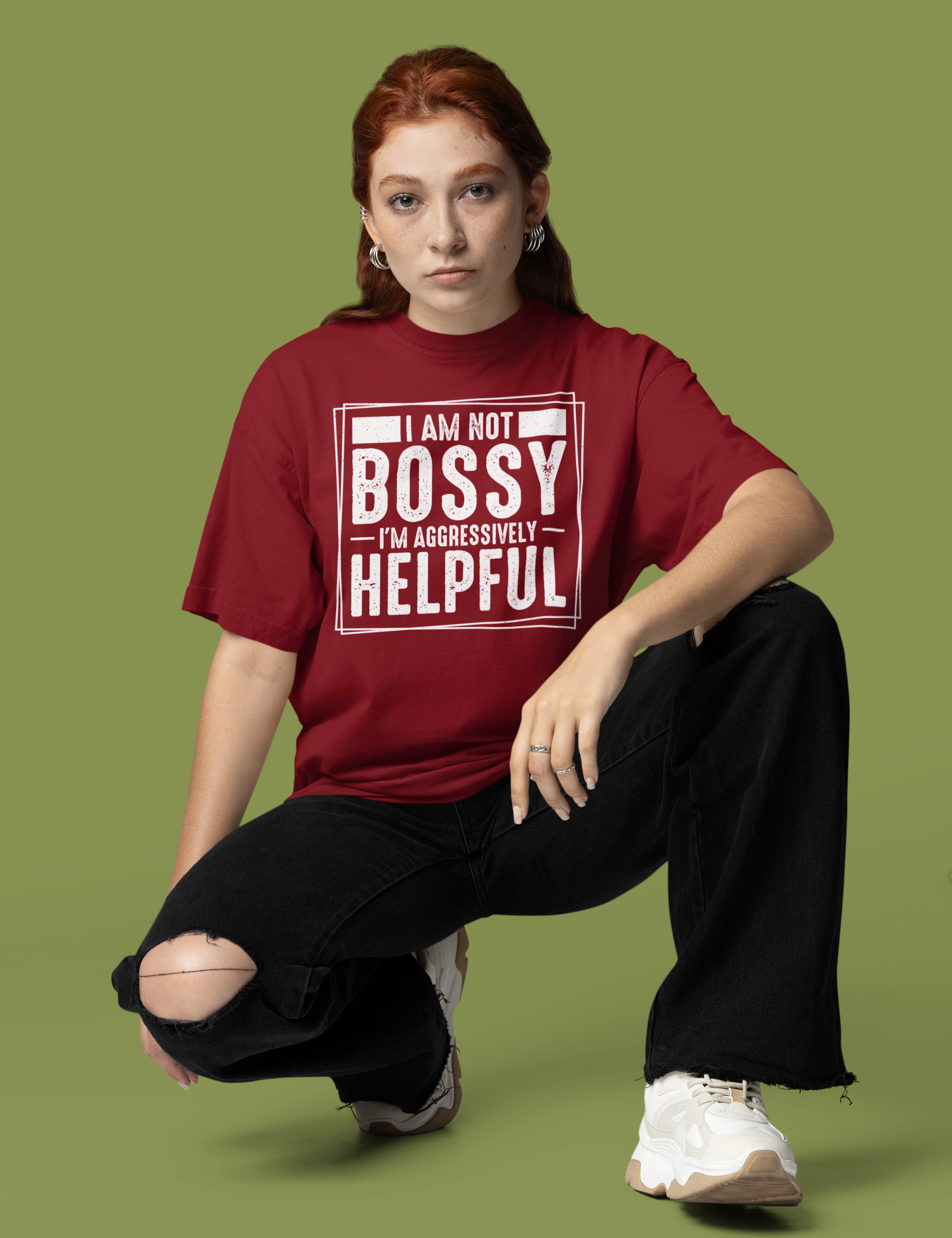 Γυναίκα φοράει μπορντό oversized t-shirt με λευκό τύπωμα “I Am Not Bossy, I’m Aggressively Helpful” και κάθεται σε στούντιο με πράσινο φόντο