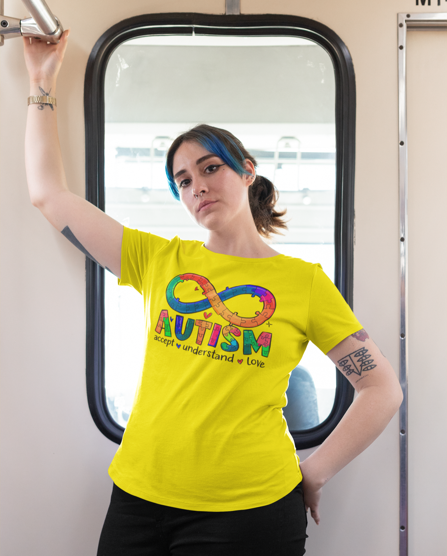 Γυναίκα με κίτρινο μπλουζάκι που γράφει "Autism Accept Understand Love" και σχέδιο άπειρο με κομμάτια παζλ, μέσα σε βαγόνι τρένου.