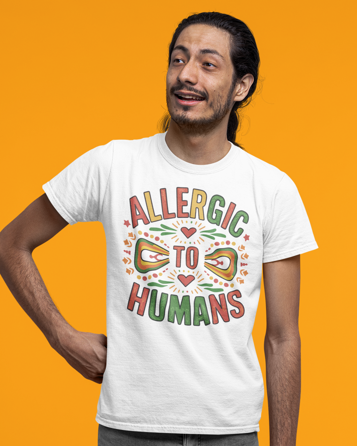 Άνδρας με μακριά μαλλιά φοράει λευκό t-shirt με τη φράση "Allergic to Humans" σε πολύχρωμο tribal σχέδιο, μπροστά σε πορτοκαλί φόντο.