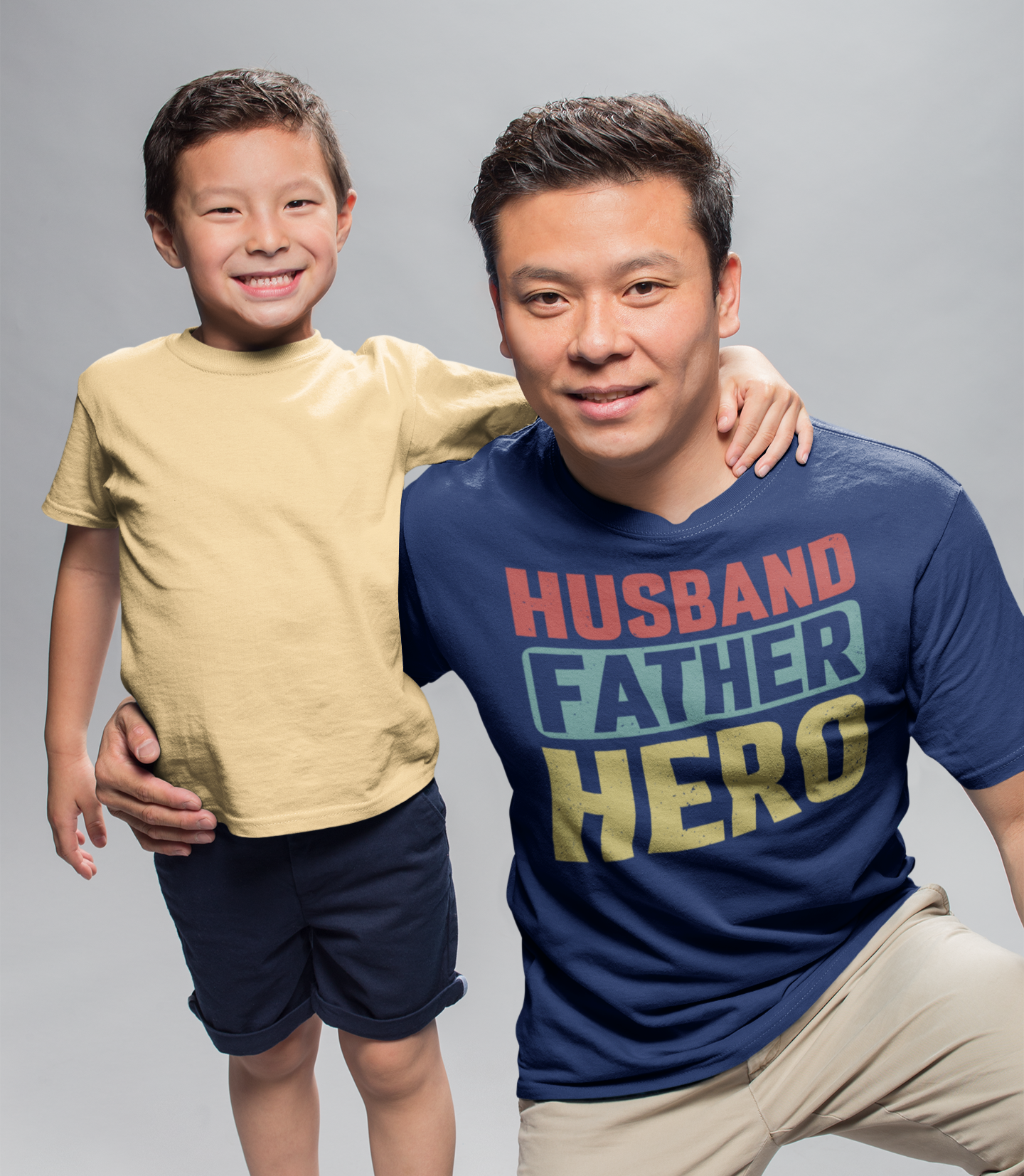 Πατέρας και γιος ποζάρουν χαμογελαστοί σε στούντιο. Ο πατέρας φοράει μπλουζάκι με το μήνυμα “Husband. Father. Hero.” σε κόκκινο, μπλε και κίτρινο χρώμα.