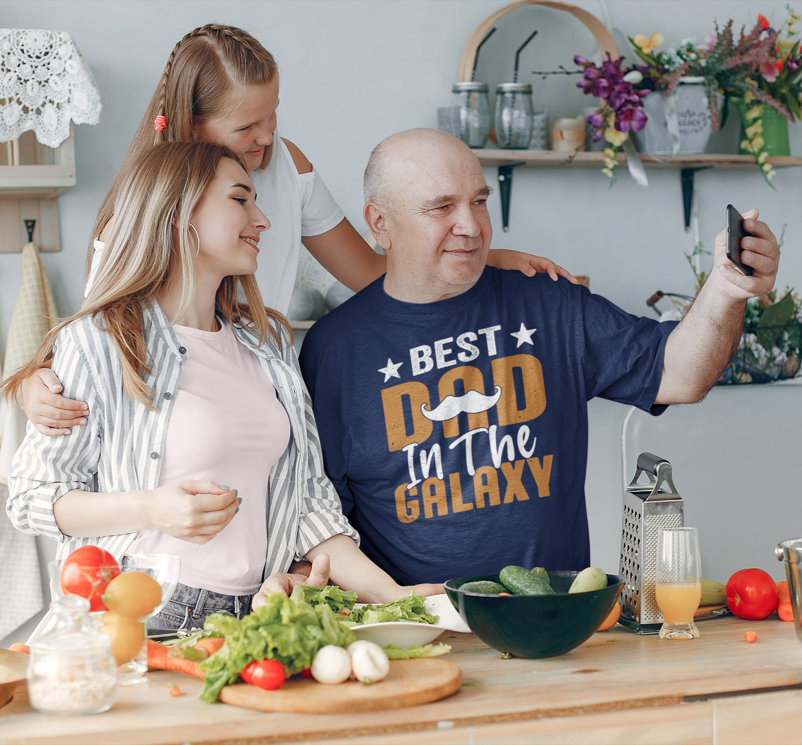Μπλουζάκι με στάμπα “Best Dad in the Galaxy” φορεμένο από παππού που βγάζει selfie με την οικογένειά του στην κουζίνα