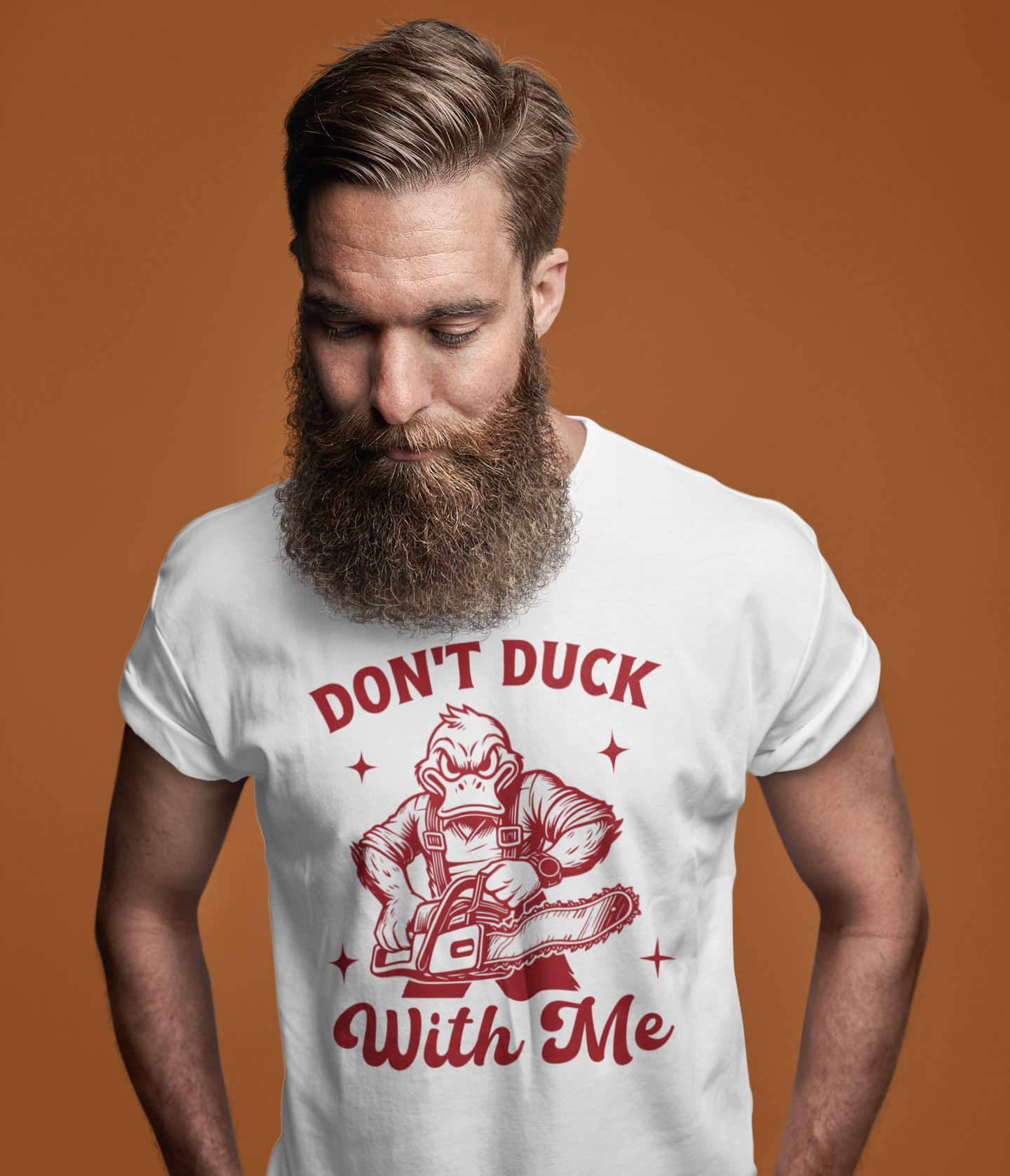 Άντρας με μακριά γενειάδα φοράει λευκή μπλούζα με κόκκινο σχέδιο που δείχνει έναν θυμωμένο πάπιο με αλυσοπρίονο και το χιουμοριστικό μήνυμα "Don't Duck With Me", μπροστά σε πορτοκαλί φόντο.