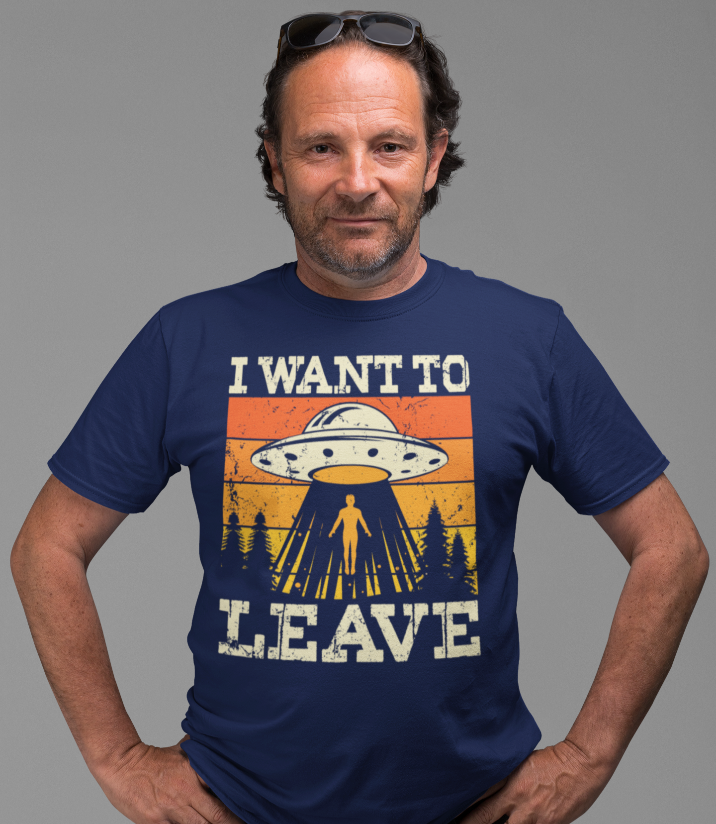 Άντρας με μπλε μπλουζάκι που γράφει “I want to leave” και δείχνει έναν άνθρωπο να απάγεται από UFO με ρετρό σχεδιασμό σε φόντο δάσους.