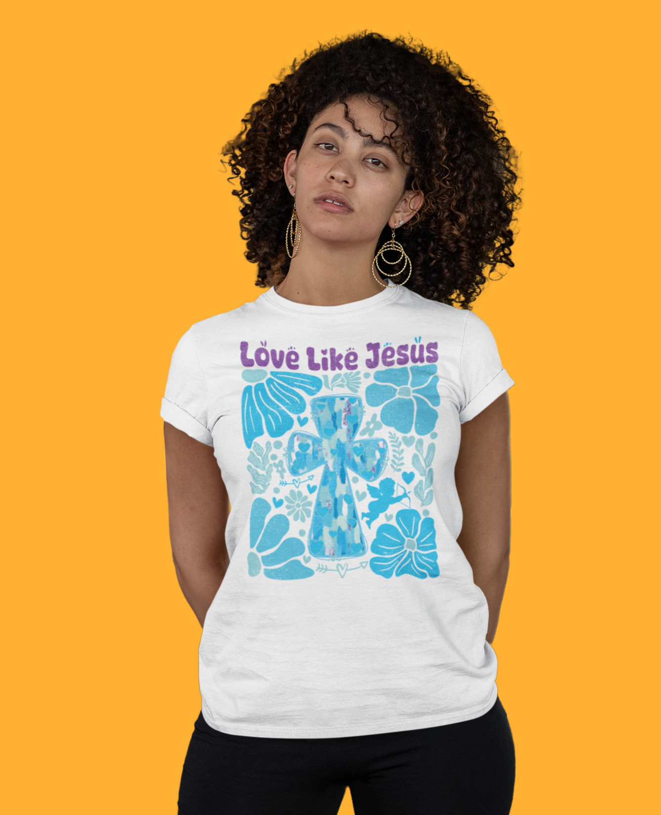 Γυναίκα με λευκό μπλουζάκι που γράφει "Love Like Jesus" και έχει μπλε σχέδιο με σταυρό και λουλούδια, σε πορτοκαλί φόντο.