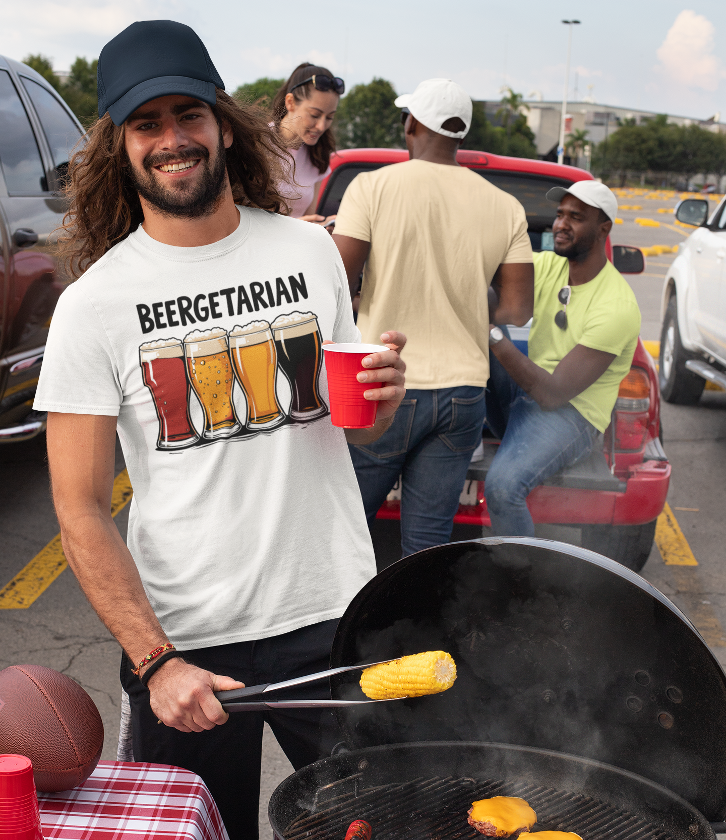 Άνδρας με καπέλο και μπλουζάκι “Beergetarian” χαμογελά ενώ ψήνει στο BBQ σε tailgate πάρτι, κρατώντας καλαμπόκι και ποτήρι σε κόκκινο κύπελλο.